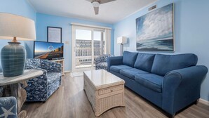 Un salon avec un canapé bleu, un fauteuil à motifs, une table basse et un ventilateur de plafond.