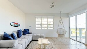 Una sala de estar moderna con un sofá seccional gris, una mesa de centro blanca, un sillón colgante y un amplio ventanal con persianas.