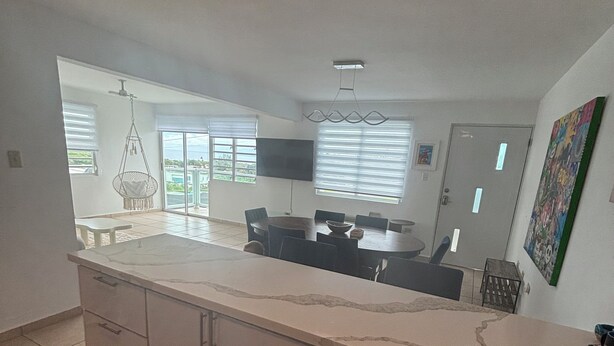 Una cocina amplia con una isla grande, un comedor con una mesa redonda y vistas al exterior a través de amplias ventanas.
