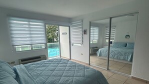 Un dormitorio con una cama, un ventanal grande, una puerta corrediza a un balcón y una lámpara en el techo.