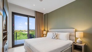 A hotel room with a large bed, two bedside lamps, a nightstand, a sliding glass door to a balcony, and a television on the left wall. - Aruba Haven: 2BR Condo w/ Balcony near Beaches (Noord)