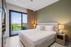 A hotel room with a large bed, two bedside lamps, a nightstand, a sliding glass door to a balcony, and a television on the left wall. - Aruba Haven: 2BR Condo w/ Balcony near Beaches (Noord)