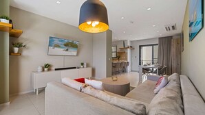 A modern living room with a sofa, a dining area, and a kitchen in the background. - Aruba Haven: 2BR Condo w/ Balcony near Beaches (Noord)