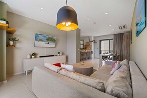 A modern living room with a sofa, a dining area, and a kitchen in the background. - Aruba Haven: 2BR Condo w/ Balcony near Beaches (Noord)