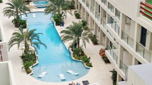 A multi-level hotel with a central swimming pool surrounded by palm trees and lounge chairs.