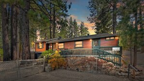 A rustic cabin with a stone foundation, wooden exterior, and a green staircase leading to a porch. - Forest Cottage · Hot Tub · Firepit · Fenced Yard (Big Bear Lake)