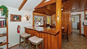 A rustic wooden interior with a bar area, wooden beams, a bookshelf, and a fire extinguisher. - Forest Cottage · Hot Tub · Firepit · Fenced Yard (Big Bear Lake)
