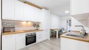 Une cuisine moderne avec des meubles blancs, un four encastré et un coin repas comprenant une table et des chaises.