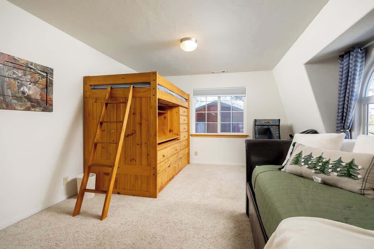 A room with a loft bed, a ladder, a window, and a green bedspread.