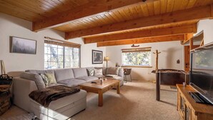 A cozy living room with a wooden ceiling, a large window, a sofa, a coffee table, and a television.