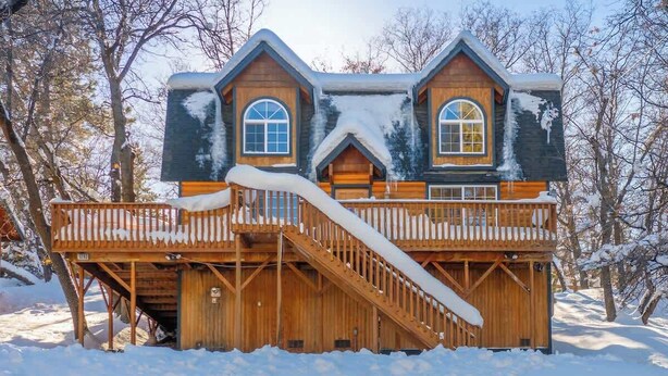 A wooden cabin with a balcony and a staircase, surrounded by snow.