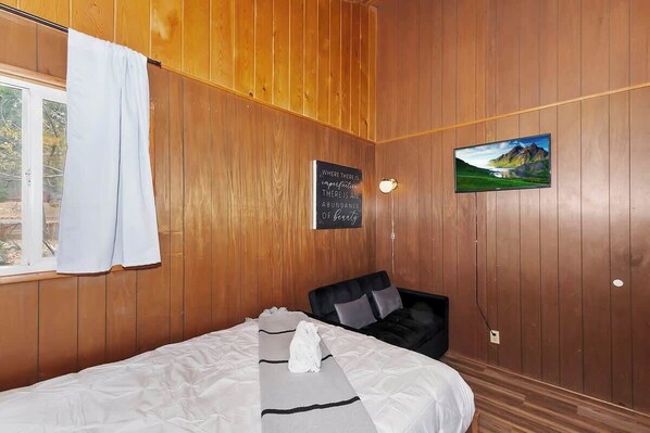 A wooden-paneled room with a bed, a black chair, a painting, and a motivational quote on the wall.
