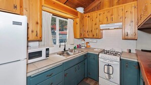 Una cocina compacta con armarios de madera, un refrigerador blanco, microondas, lavaplatos, estufa y una ventana con cortinas.