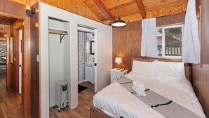 Un dormitorio con paneles de madera, una cama, una mesita de noche y un ventanal con cortinas.