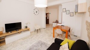 A modern living room with a flat-screen TV, a wooden coffee table, a sofa with cushions, and a dining area with a wooden table and chairs. - Rhome Suite Vatican APTS (ROMA)