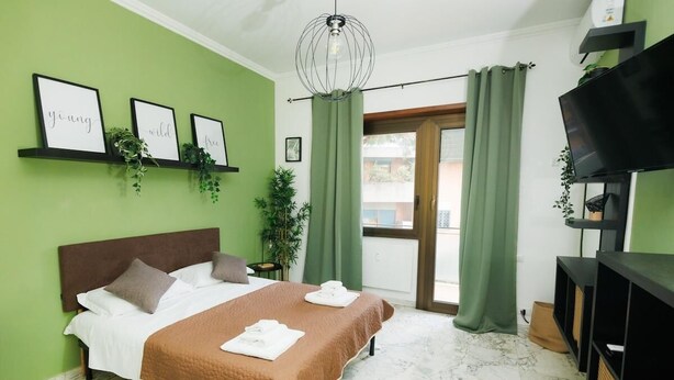 A bedroom with a bed, green curtains, a TV, and framed pictures on the wall. - Rhome Suite Vatican APTS (ROMA)