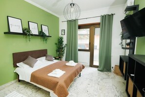 Een slaapkamer met een bed, groene gordijnen, een televisie en ingelijste foto’s aan de muur.