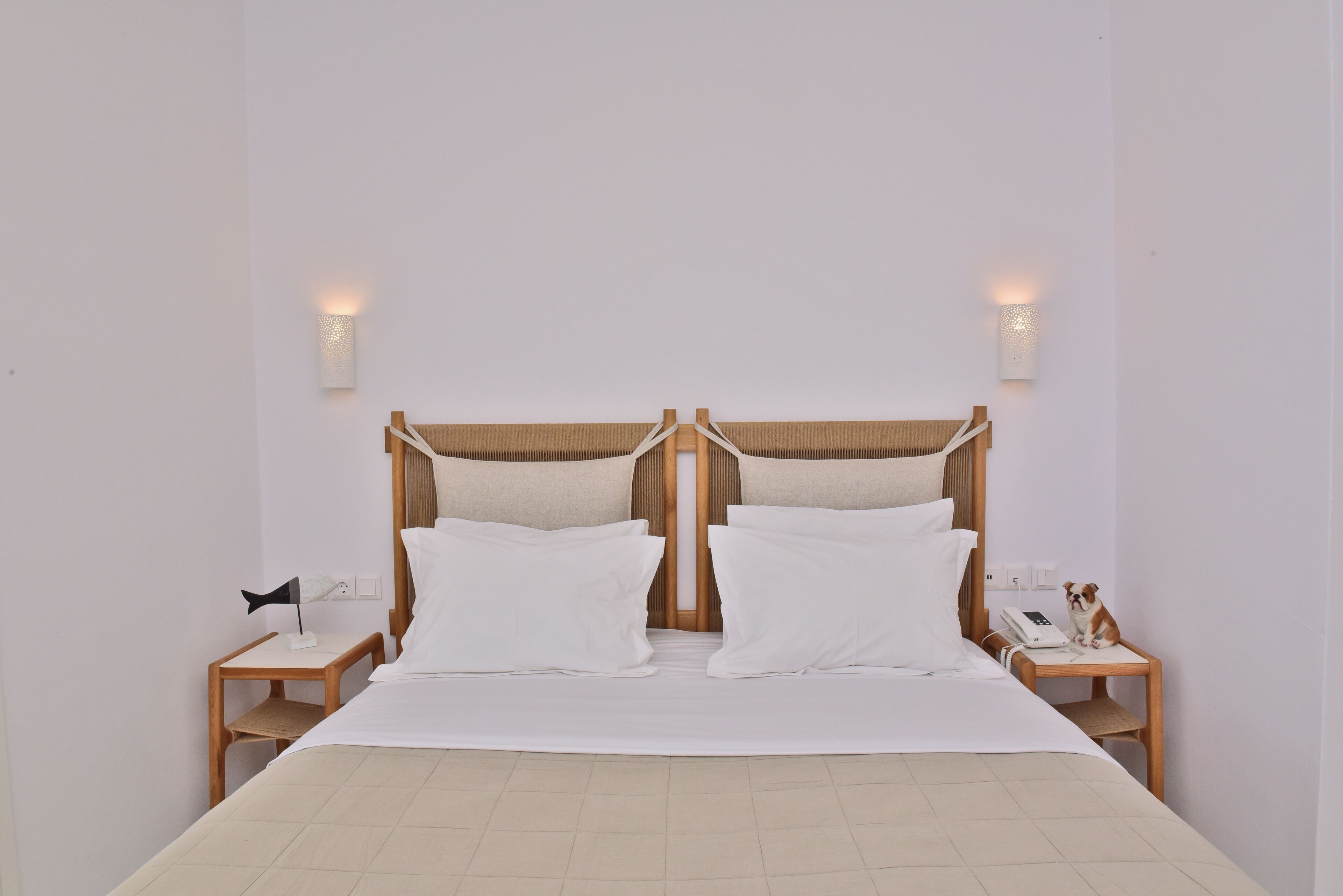 Una cama bien tendida con sábanas blancas, dos mesitas de noche con lámparas y un cabecero de madera.