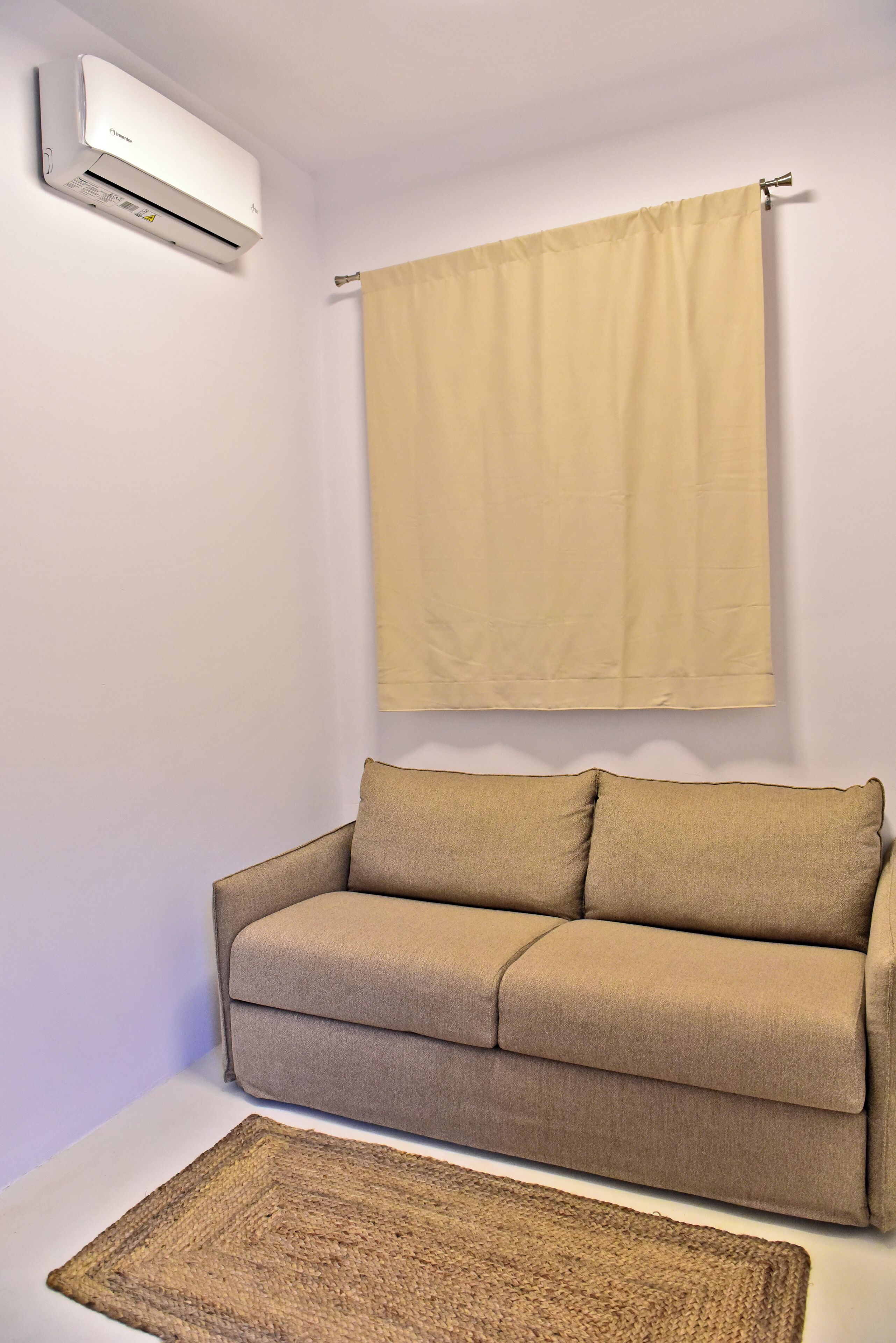 A room with a beige sofa, a beige curtain, and a white air conditioning unit.