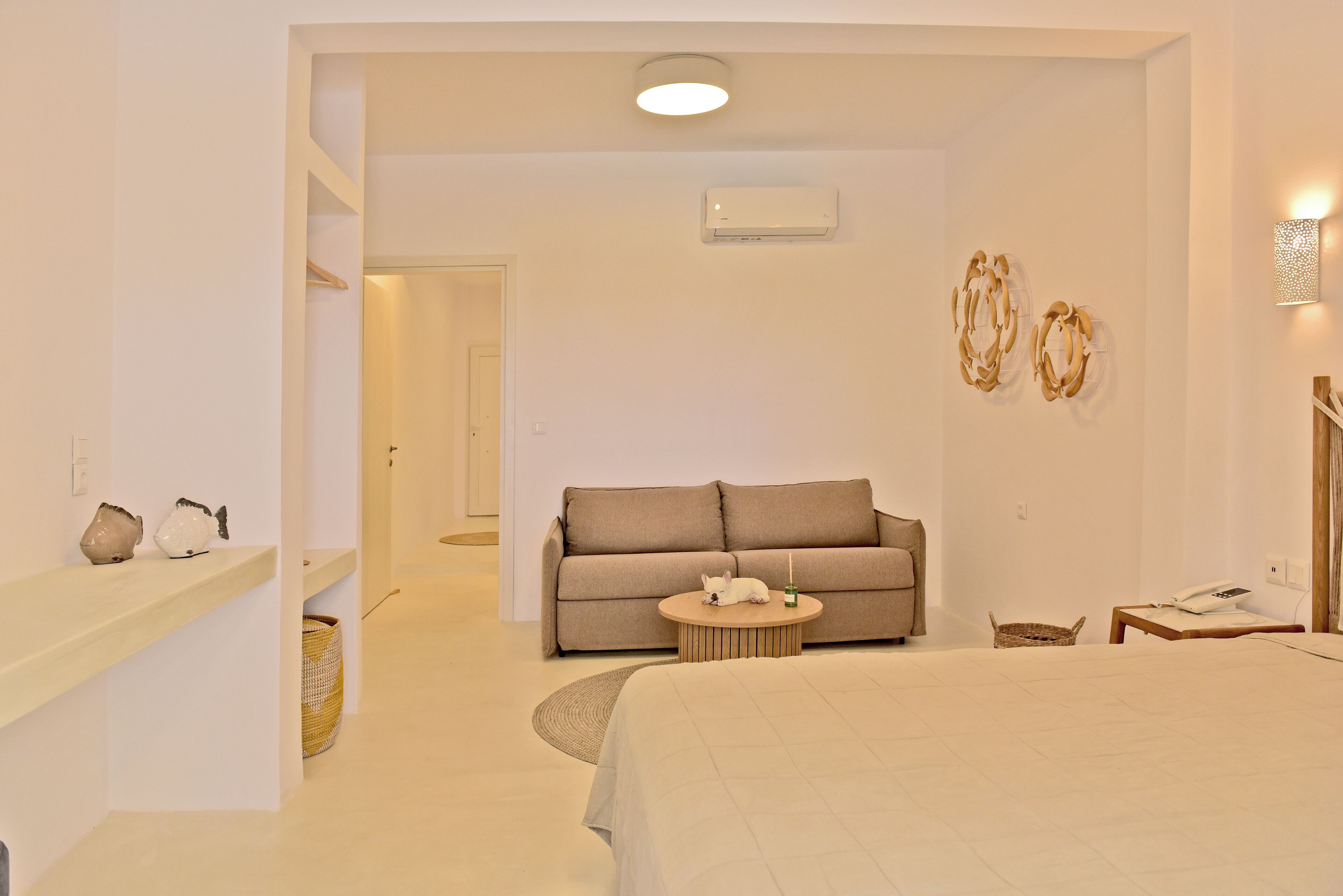 A hotel room with a bed, a sofa, a small round table, and a wall-mounted air conditioner.