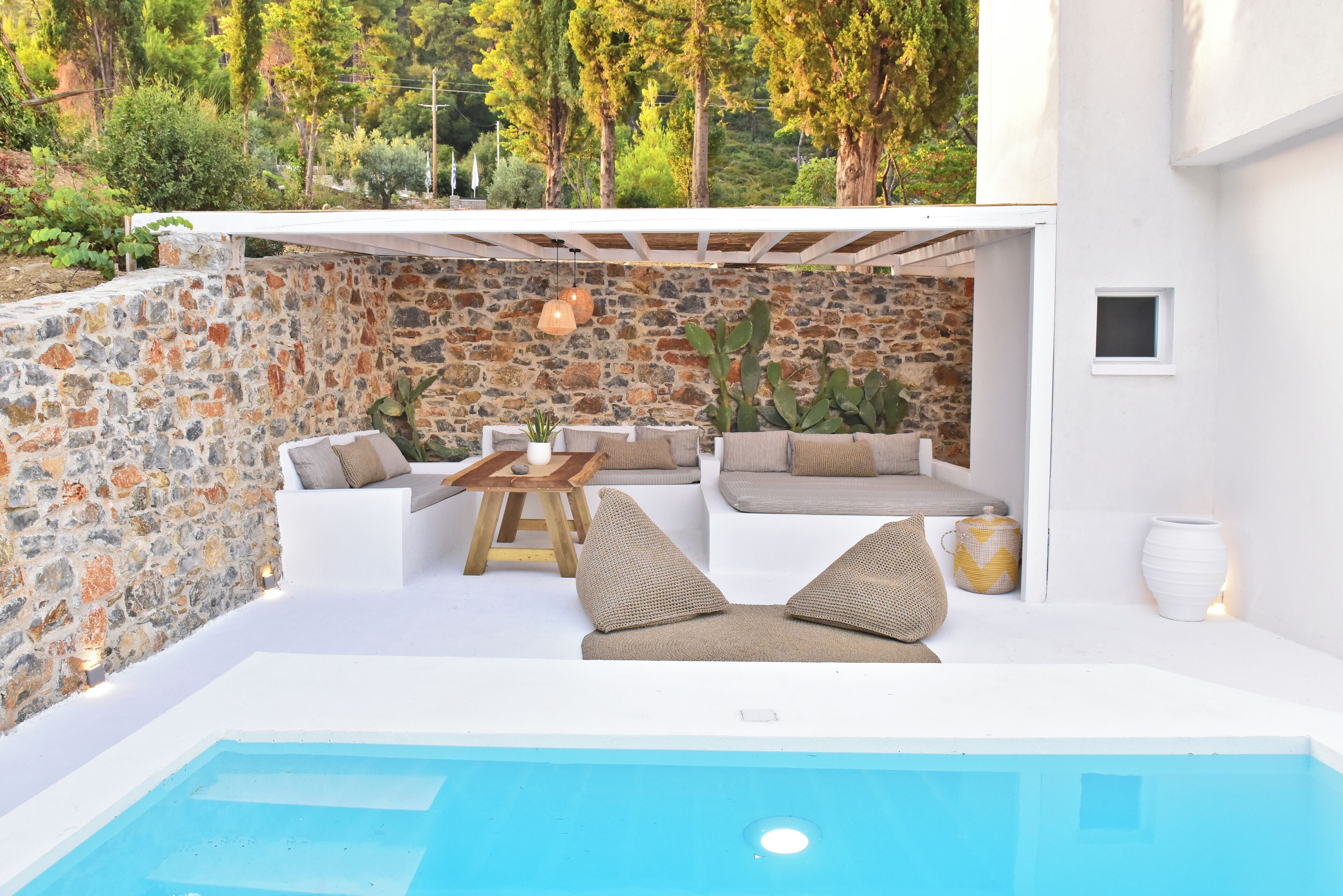 Un espace piscine extérieur moderne, agrémenté de murs en pierre, de mobilier blanc et d’une pergola.