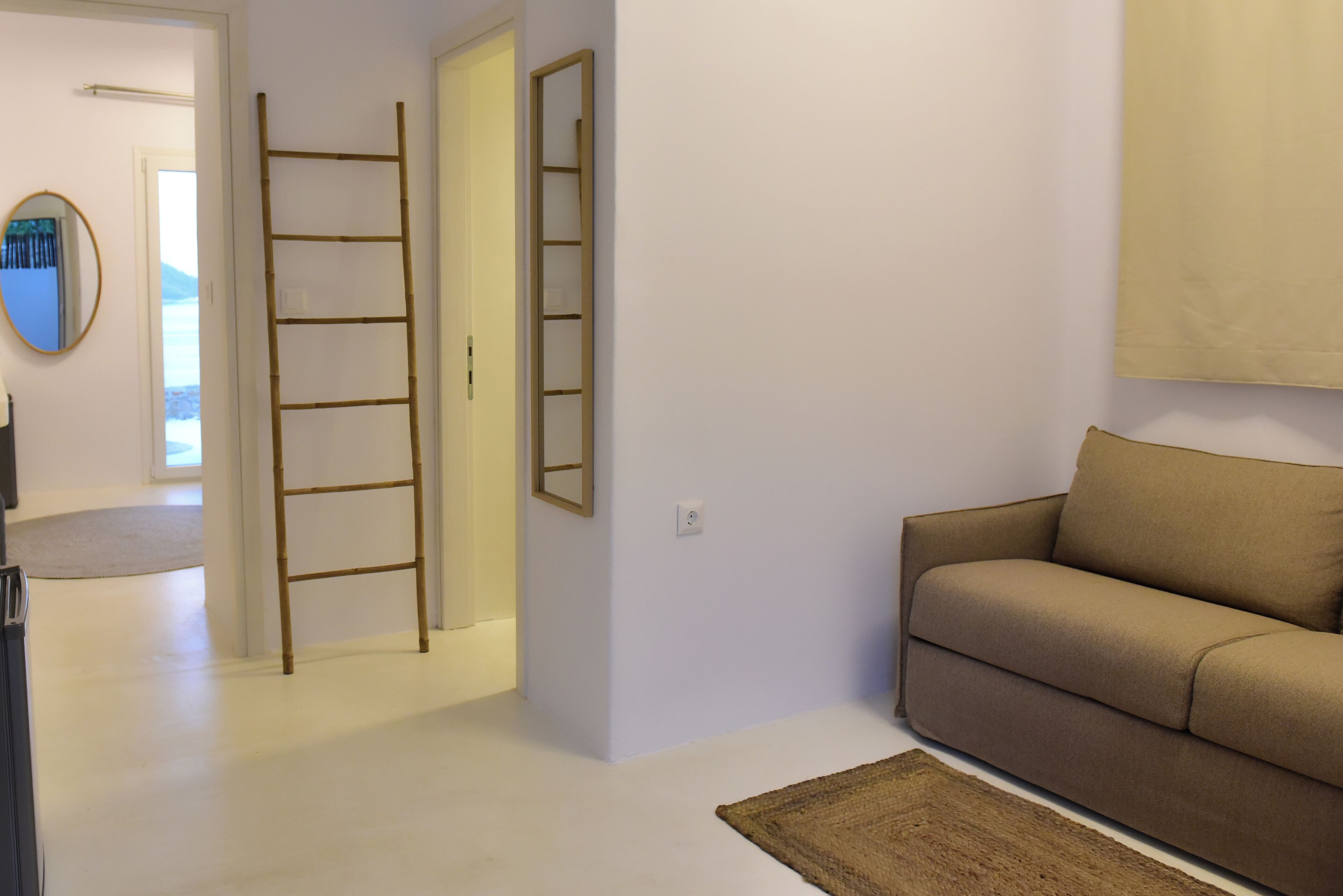 Una habitación con un sofá color beige, una escalera de madera y un espejo en la pared.