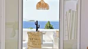 A balcony with a wicker chair, a cactus, and a view of the sea and a mountain. - Natura Luxury Villas (Skopelos)