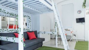 En moderne stue med en grå sofa, røde puder, en hvid stige og grønt kunstgræs.