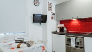 Et kompakt køkken med røde mursten som baggrund, et fladskærms-tv ophængt på væggen og et spiseområde med et bord dækket til to.