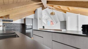 A modern kitchen with a high ceiling and exposed wooden beams, featuring a large island and built-in appliances.
