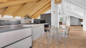 A modern kitchen with a wooden ceiling, a central island, and clear chairs around a round table.