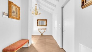 A hallway with a wooden floor, a bench, a mirror, and framed artwork on the walls.