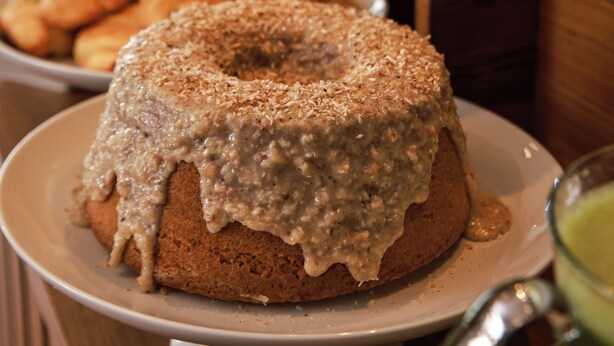 A cake with white icing and a dusting of sugar on a white plate. - Pousada Grega Noronha (Fernando de Noronha)
