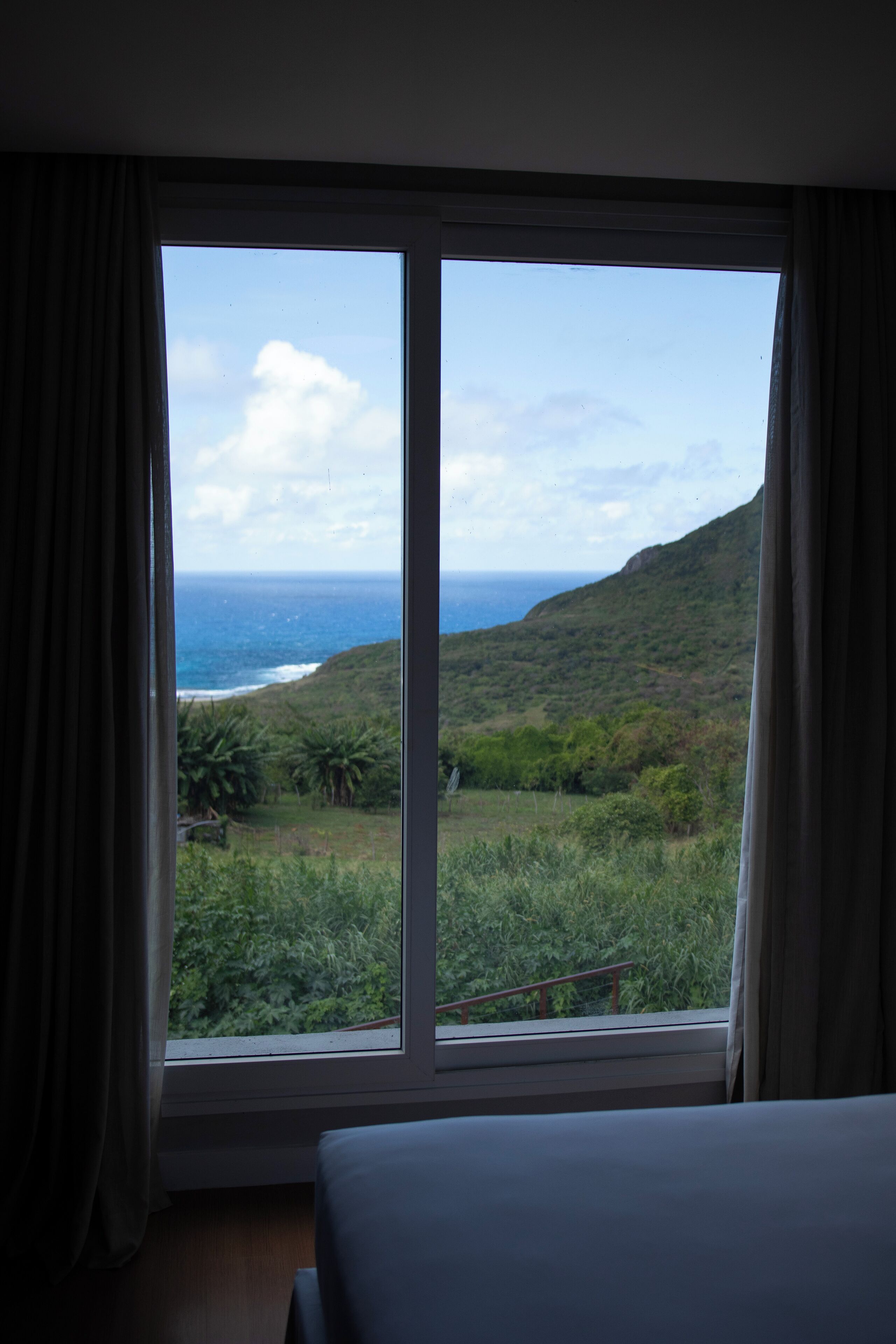 Quarto com uma grande janela que oferece vista para a paisagem costeira, incluindo o oceano e colinas.