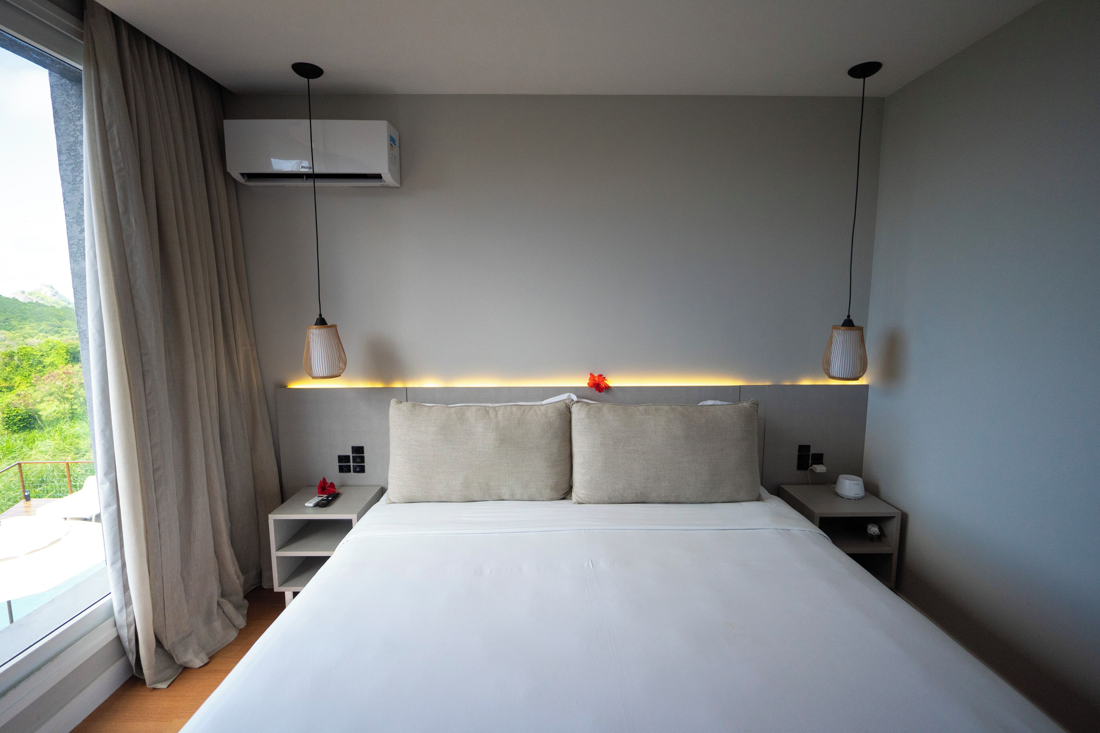 Una camera d'albergo moderna con un letto grande, due comodini, un tavolino, un condizionatore d'aria a parete e una finestra con tende.