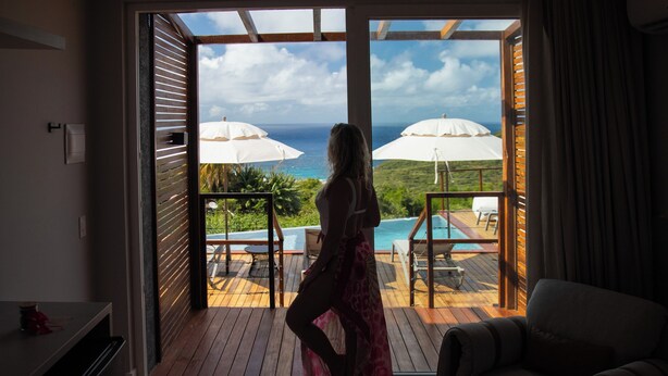 Une pièce avec vue sur une piscine et des parasols, une terrasse en bois et un canapé.