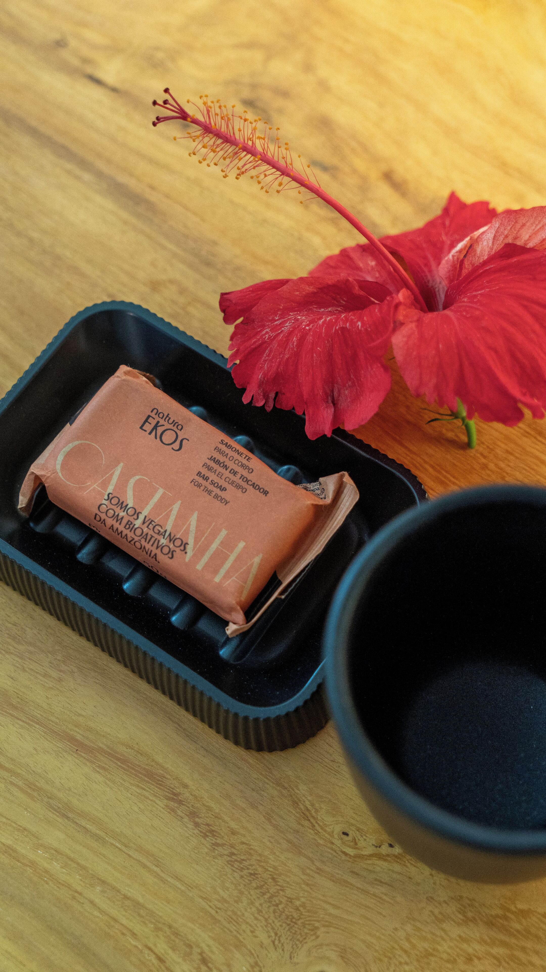 A black tray with a brown bar of soap and a red hibiscus flower on a wooden table.