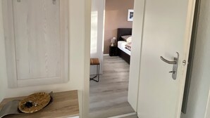 Ein Flur mit einer hölzernen Bank, einem an der Wand befestigten Kleiderhaken und einer Tür zu einem Schlafzimmer mit Bett und Nachttisch.