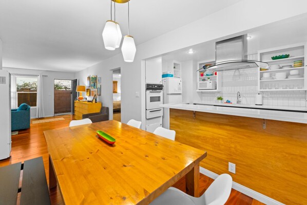 A modern kitchen with white cabinets, a wooden dining table, and pendant lighting.