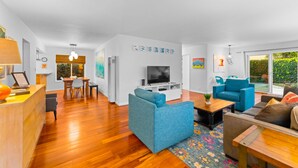 Ein modernes Wohnzimmer mit Fernseher, blauen Sofas, Holzboden und einem Essbereich mit Tisch und Stühlen.