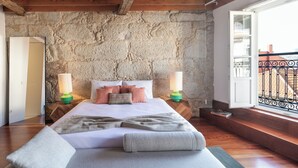 Camera da letto con parete in pietra, travi in legno, un letto grande con cuscini e vista sul balcone esterno.