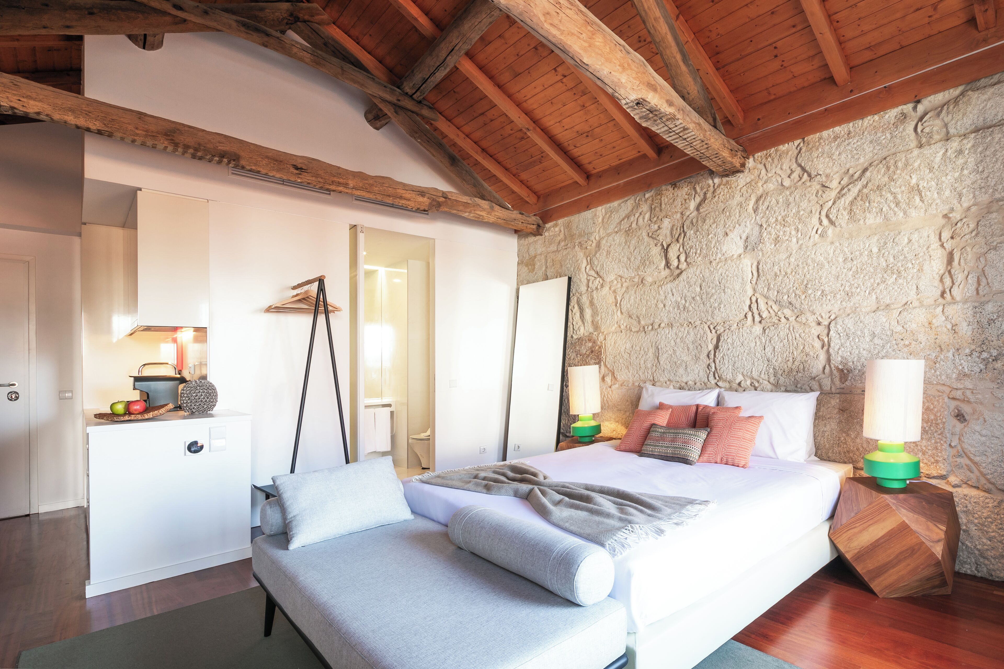 Une chambre à coucher avec un lit, des tables de chevet, une commode et un mur en pierre.