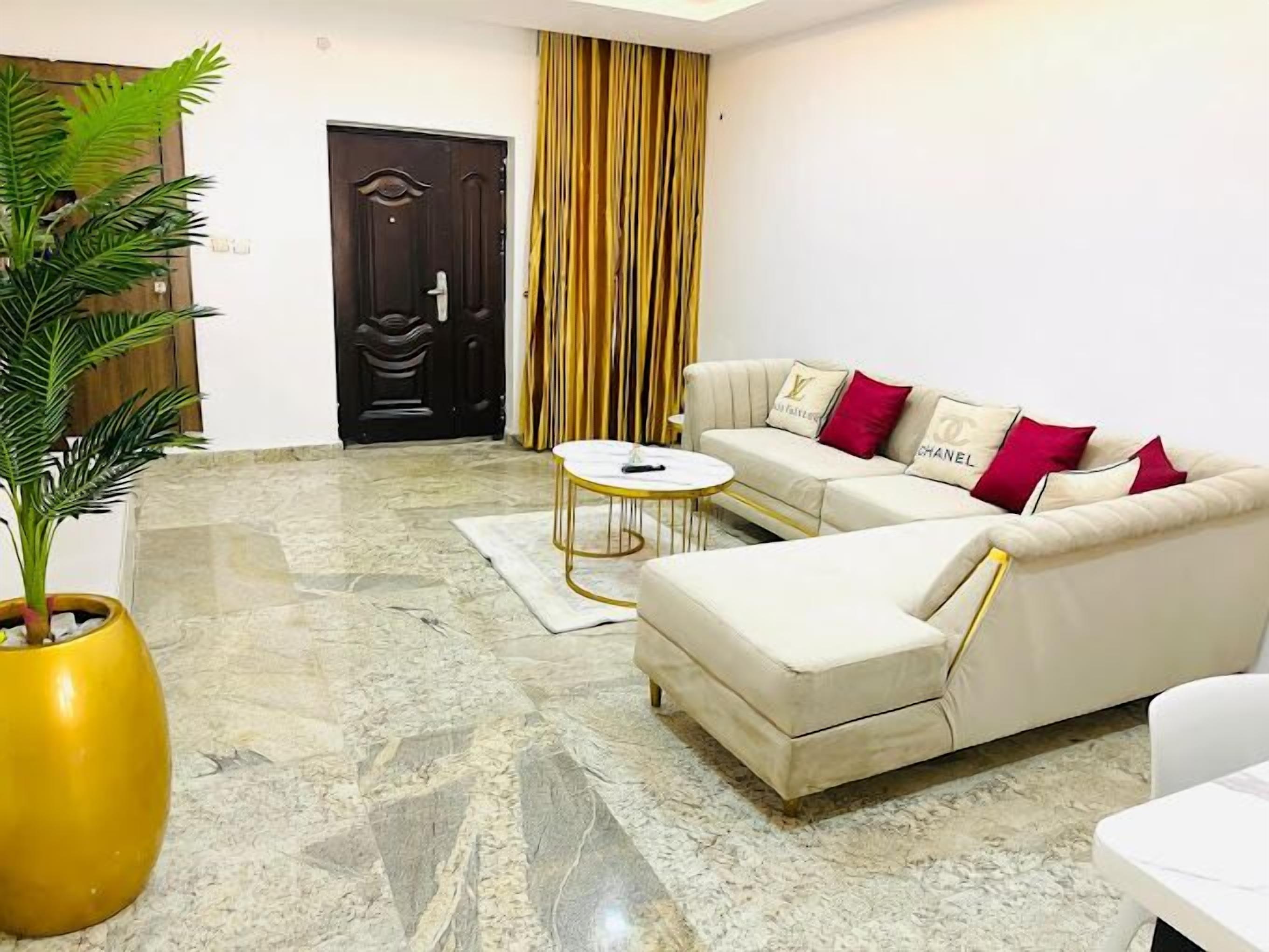 A living room with a beige sofa, a coffee table, a potted plant, and a striped curtain.