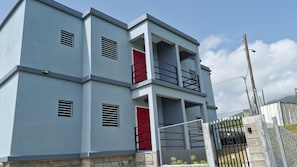 Un immeuble à plusieurs étages, doté d’une façade grise, de portes rouges et d’une entrée fermée par un portail.