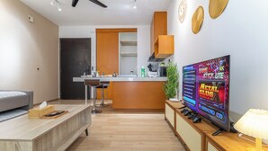 A modern living room with a sofa, a TV, and a coffee table. There is a kitchen area with a counter and cabinets. - [NEW] Private Jacuzzi | Near Velocity Mall | MRT | Retro Games (Cheras)