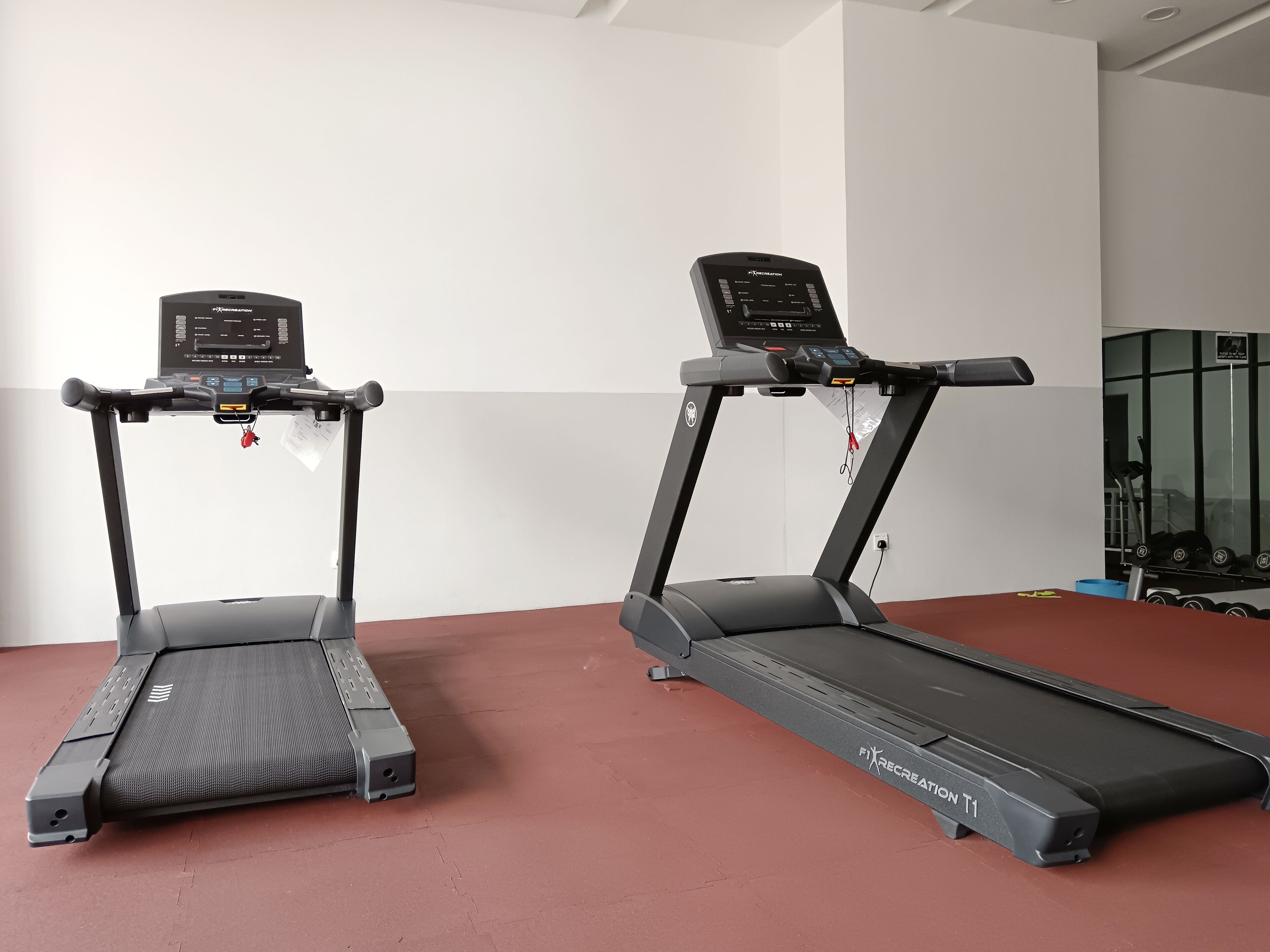 Two treadmills in a gym with a red floor and white walls.