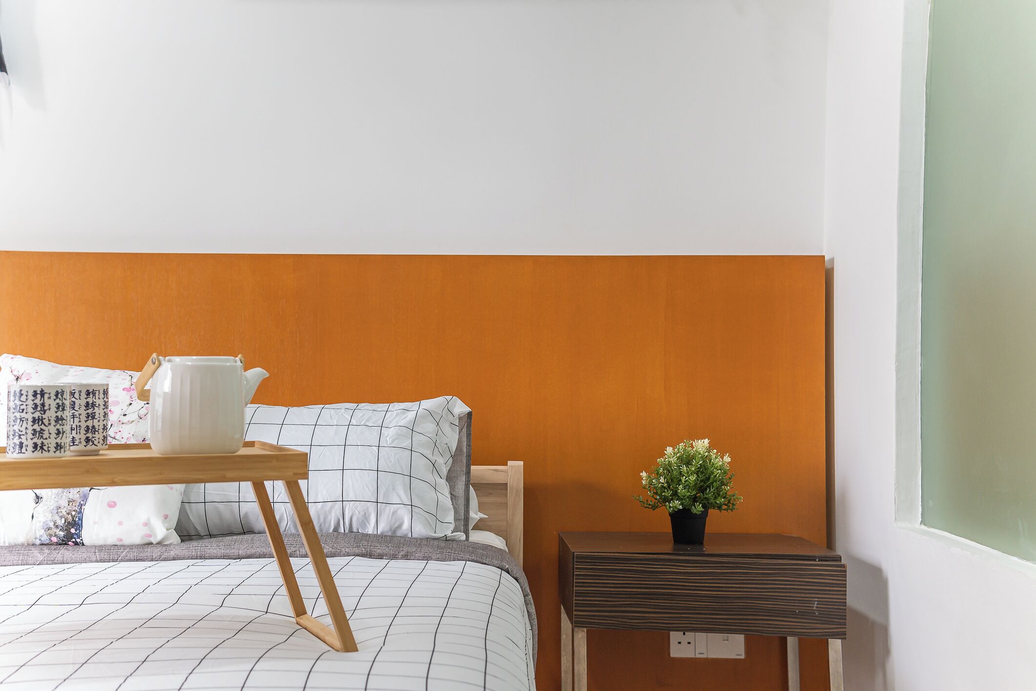 Ein ordentlich eingerichtetes Schlafzimmer mit einem Bett, einem Nachttisch mit Pflanze und einem kleinen Tisch mit Teekanne.