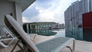 A poolside area with lounge chairs and a glass-bottomed pool reflecting buildings. - [NEW] Private Jacuzzi | Near Velocity Mall | MRT | Retro Games (Cheras)