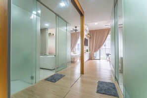 Ein moderner Hotelkorridor mit Glaswänden, Holzboden und Blick auf ein Schlafzimmer mit Bett und Vorhängen.