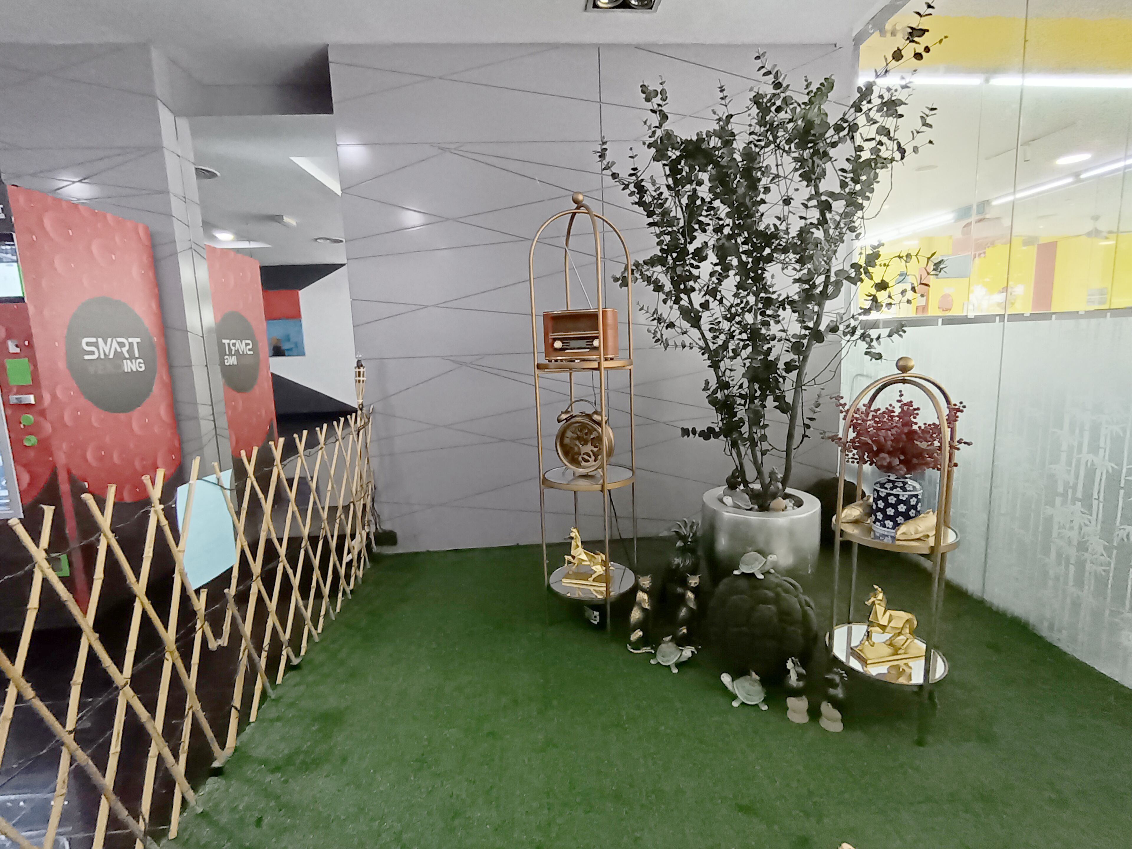 A display area with a green carpet, a metal fence, a potted plant, and various decorative items including figurines and a small shelf with a clock.